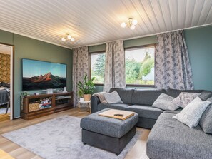 A living room with a sectional sofa, a flat-screen TV, a wooden entertainment unit, and a large window with patterned curtains. - Kiviniemi by Interhome (Kerimäki)