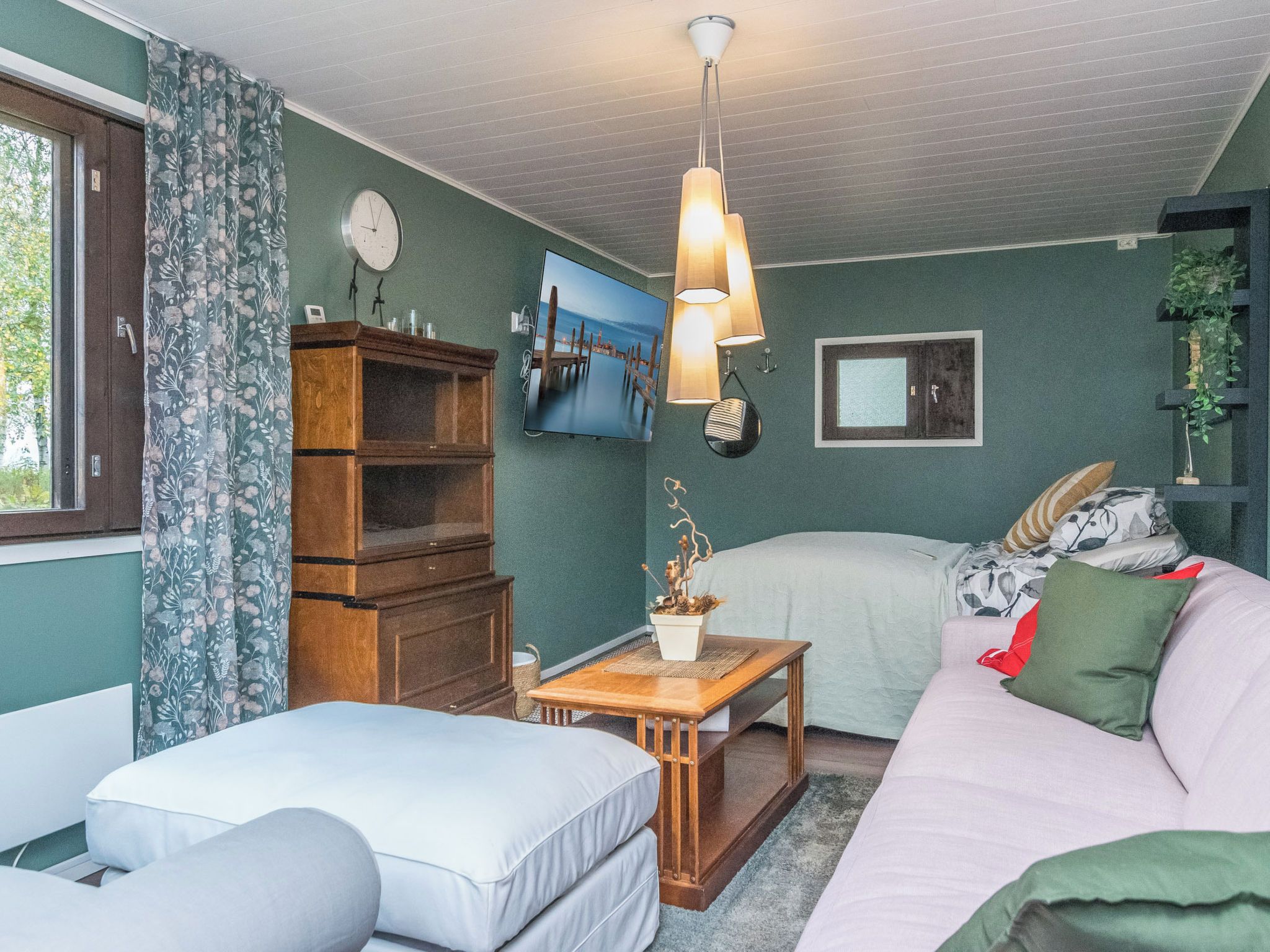 Una habitación acogedora con cama, sofá, aparador de madera, televisor y ventana con cortinas.