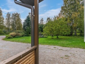 A gravel path leading to a wooden deck with a metal railing, surrounded by a grassy area with trees and shrubs. - Kiviniemi by Interhome (Kerimäki)