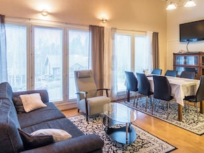 Un salon comprenant un canapé, des fauteuils, une table basse en verre et un coin repas avec une table et des chaises.