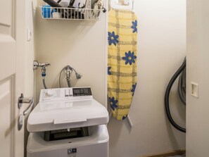 Een badkamer met een witte wasmachine, een handdoekhouder met een gele handdoek en een zwarte stofzuiger.