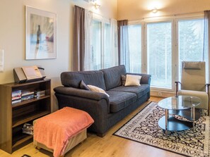 A living room with a sofa, a chair, a coffee table, a bookshelf, and a window with blinds.