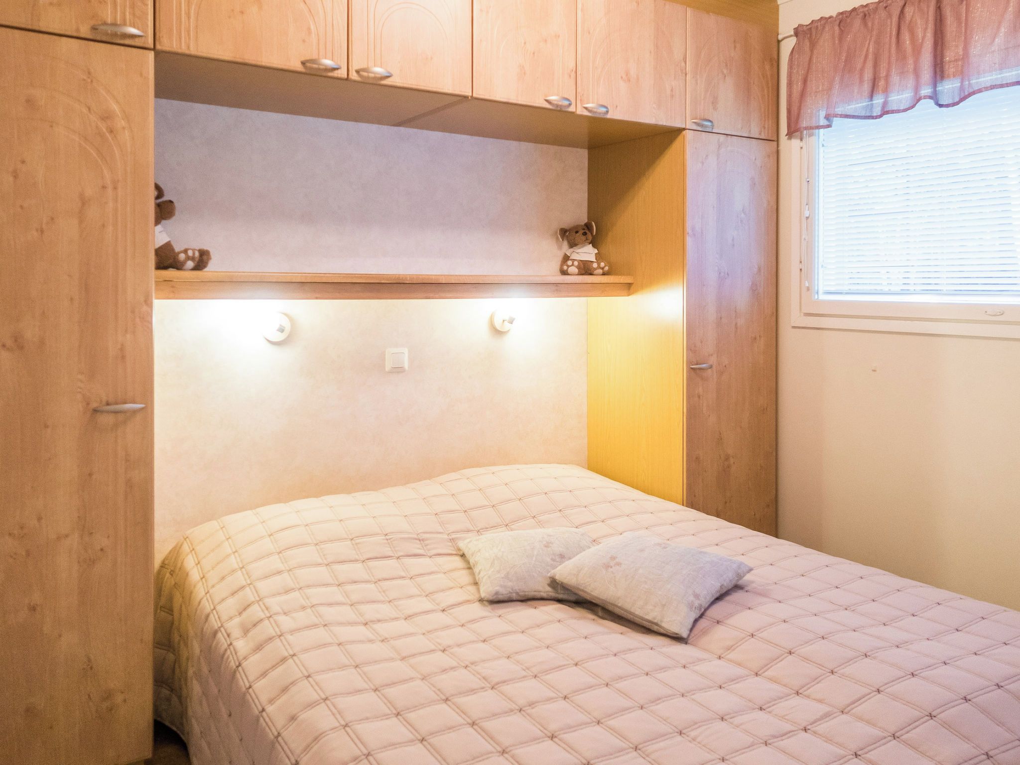Une chambre à coucher avec un lit, une armoire en bois et une fenêtre avec des stores.