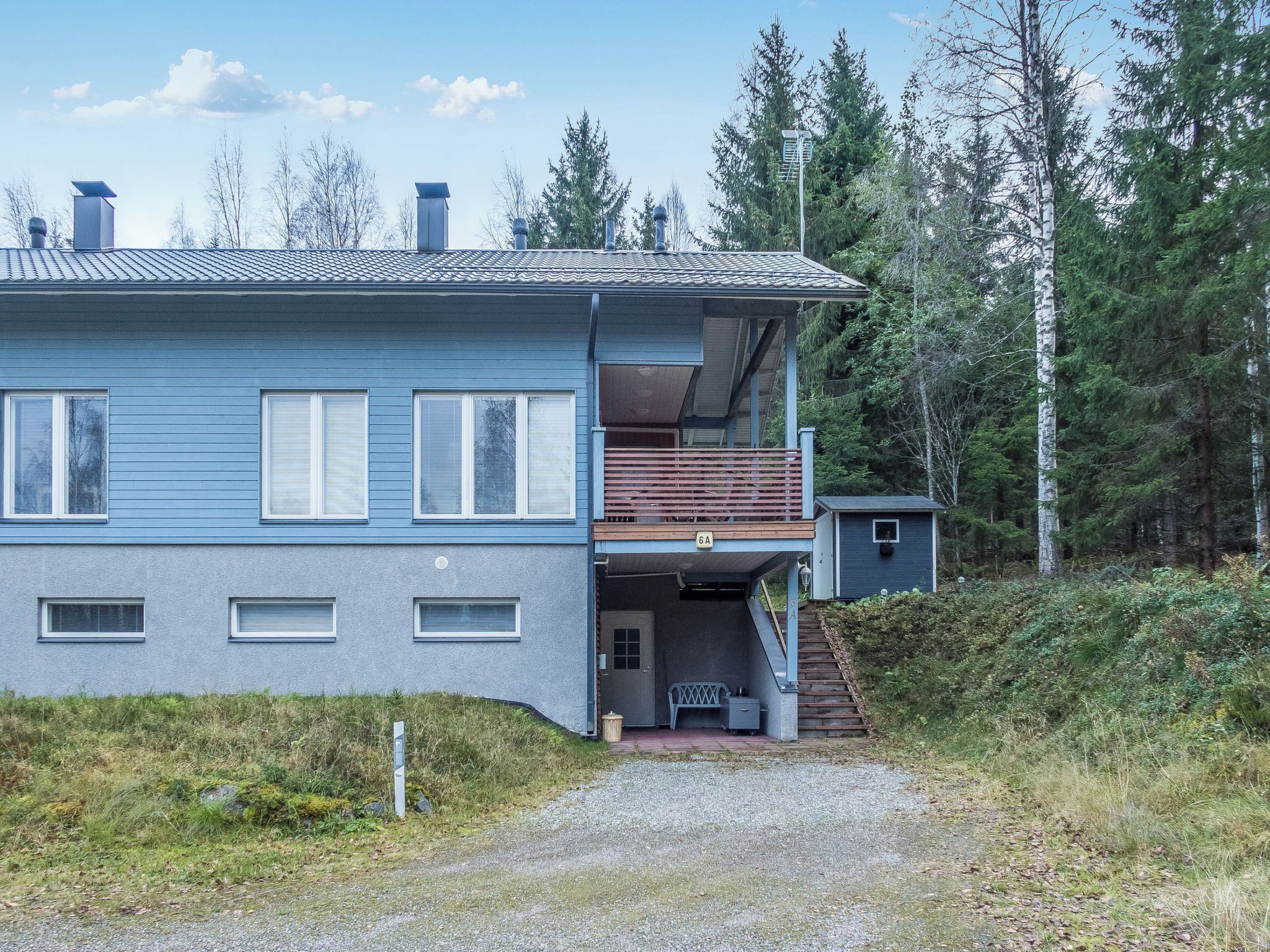 A two-story house with a balcony, a small attached structure, and a gravel driveway leading to the entrance.
