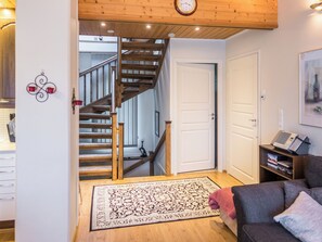 Een woonkamer met een trap, een deur, een boekenkast en een klok aan de muur.