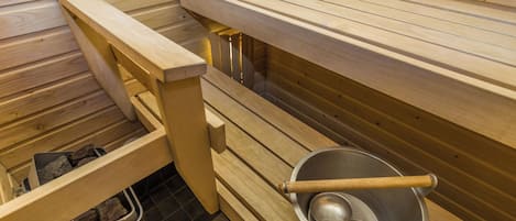 A sauna room with wooden benches, a metal basin, and a stone-filled container.