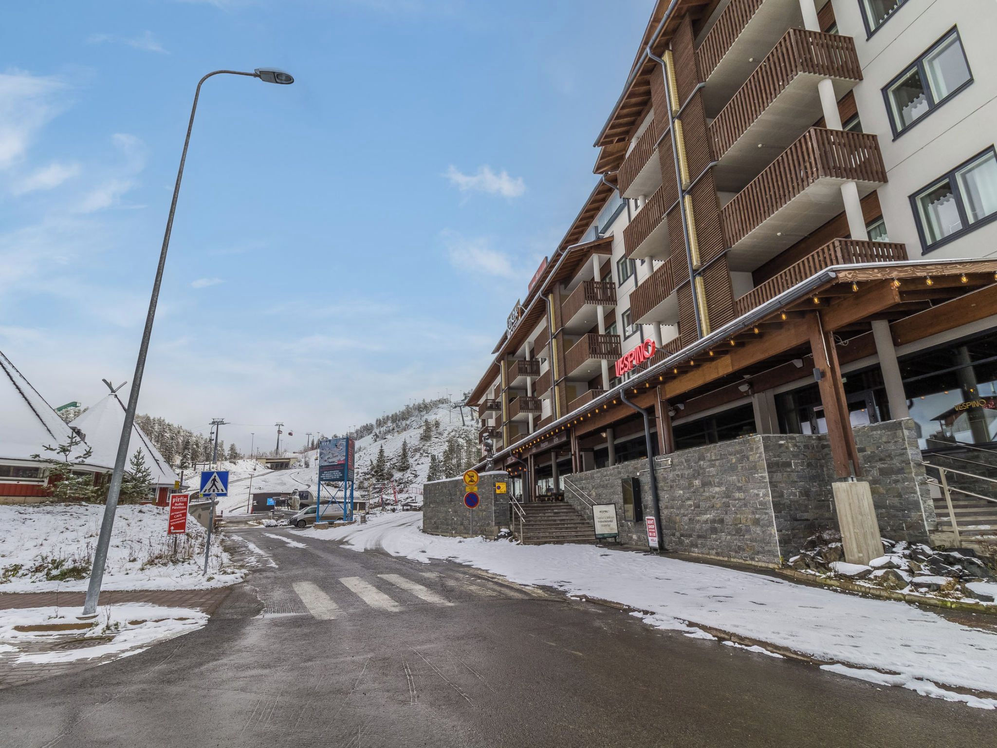 A multi-story hotel with balconies, a ski lift in the background, and a snow-covered ground.
