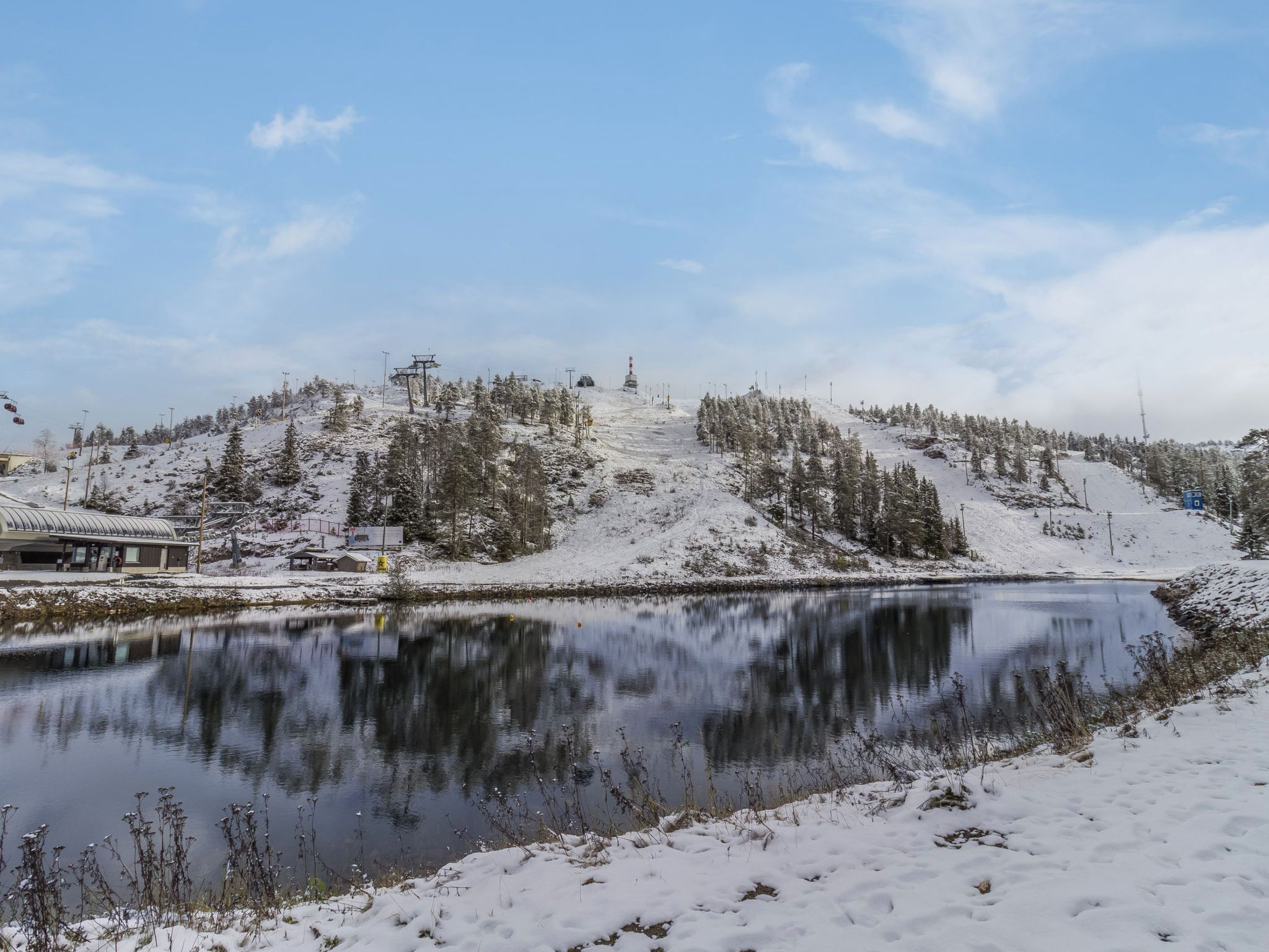 Lumipeitteinen maisema, jossa on järvi, puita ja hiihtohissi.