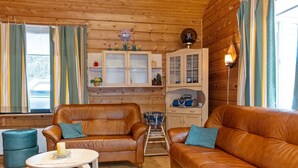 A cozy cabin interior with two leather sofas, a small wooden table, and a kitchen area with cabinets and a radio.