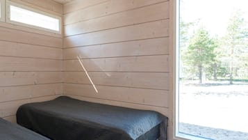 A room with two beds, wooden walls, and a large window.