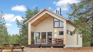 A cabin with a wooden exterior, large windows, and a covered porch with a picnic table.