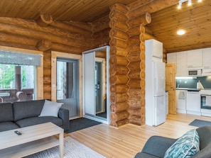 L’intérieur d’une cabane en rondins comprend un canapé, une table à manger, un coin cuisine et une porte donnant sur un balcon.