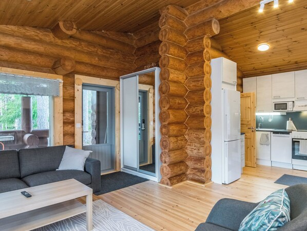 A log cabin interior with a sofa, a dining table, a kitchen area, and a door leading to a balcony.