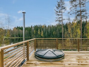 A wooden deck with a sauna, surrounded by a forest and a lake.