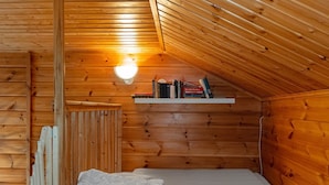 A small, cozy wooden room with a sloped ceiling, a single bed with white bedding, a shelf with books, and a wall-mounted light fixture. - Aisakello by Interhome (Kittilä)