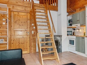 A wooden staircase leading to an upper level, a kitchen with modern appliances, and a fireplace. - Aisakello by Interhome (Kittilä)
