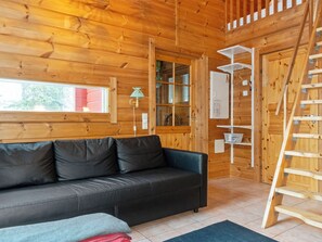 Interior de uma cabana de madeira com sofá, janela, luminária e escada de madeira.
