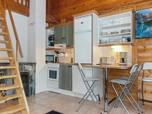 Cozinha compacta com forno embutido, geladeira e área de refeições com mesa e cadeiras.