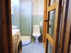 Et lille badeværelse med vaskemaskine, toilet og bruseniche.