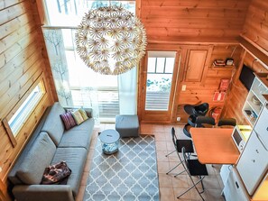 Indbydende hyttekøkken med sofa, skammel, spisebord, stole, hængende lampe og et køkkenområde.