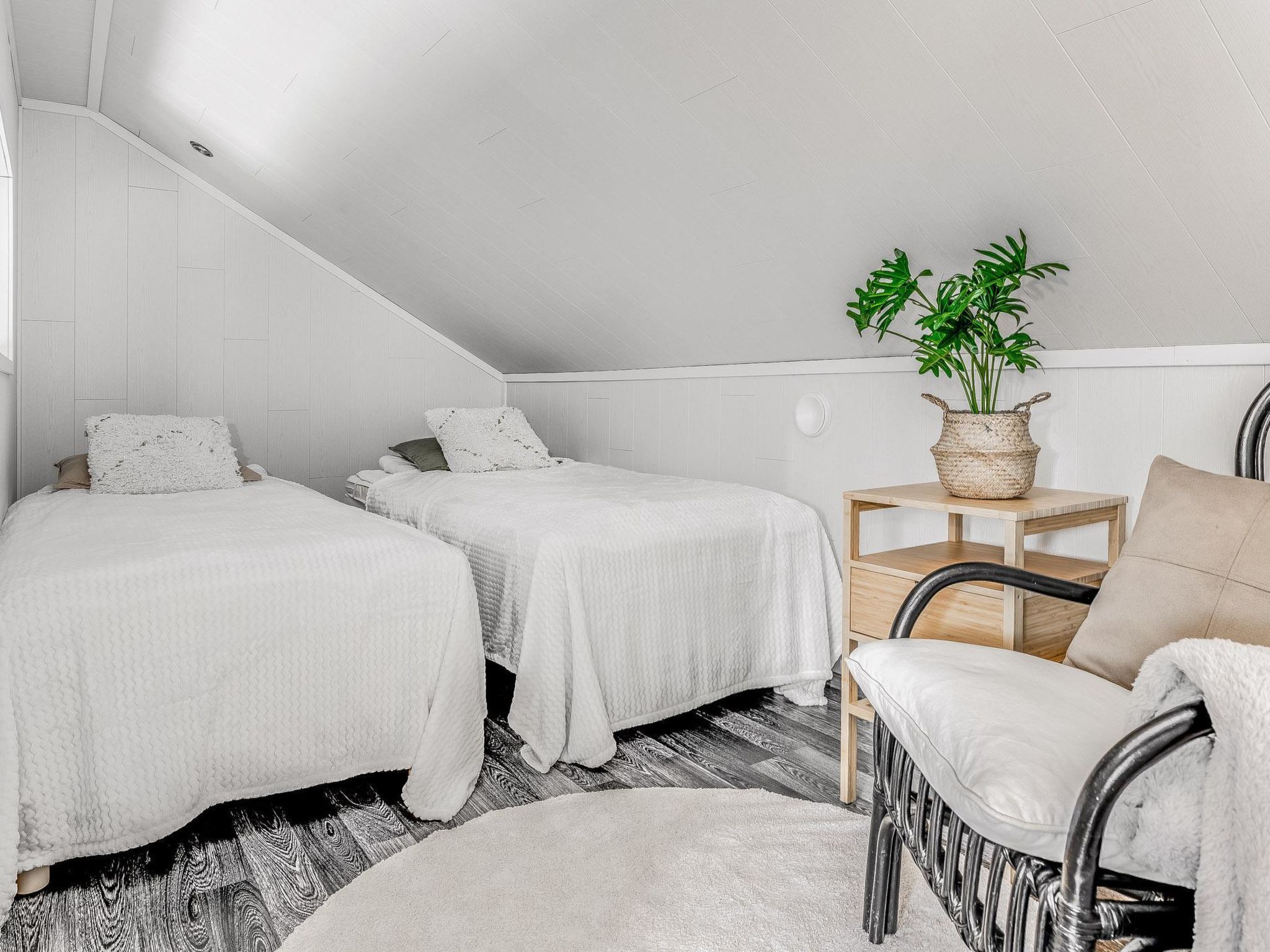 Une chambre avec deux lits, une table de chevet en bois, une chaise et une plante en pot.