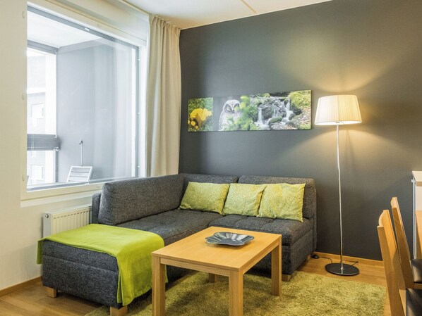 A modern living room with a grey sofa, green cushions, a wooden coffee table, and a floor lamp.