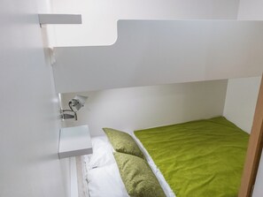 Ein Etagenbett mit einer grünen Matratze, einem weißen Kissen und einem kleinen Nachttisch mit einer Lampe.