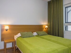 A hotel room with a wooden headboard, two bedside lamps, a green bedspread, and a window with curtains. - Levi chalets 1602 by Interhome (Kittilä)