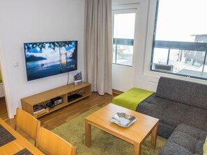 Ein modernes Wohnzimmer mit Flachbildfernseher, Holzmöbeln, einer grünen Decke und Blick auf die Stadt durch große Fenster.