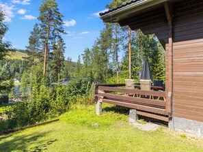 A wooden deck with outdoor furniture, overlooking a forested area and a body of water.