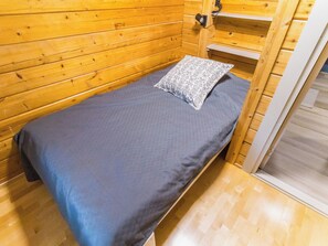 Un letto singolo con un materasso grigio e un cuscino a motivi in una stanza in legno con pavimento in legno.