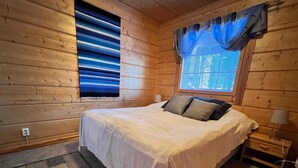 Une chambre à coucher dans une cabane en bois, avec un lit, une table de chevet, une lampe et une fenêtre ornée de rideaux bleus.
