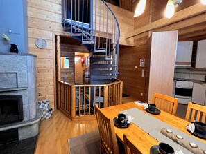 A compact kitchen with a built-in stove, a dining area with a wooden table and chairs, and a spiral staircase leading to an upper level. - Jytilevi b by Interhome (Kittilä)