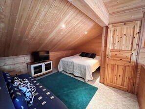A small, cozy room with a sloped ceiling, a bed with a white bedspread, a television on a wooden cabinet, and a green rug on the floor. - Jytilevi b by Interhome (Kittilä)