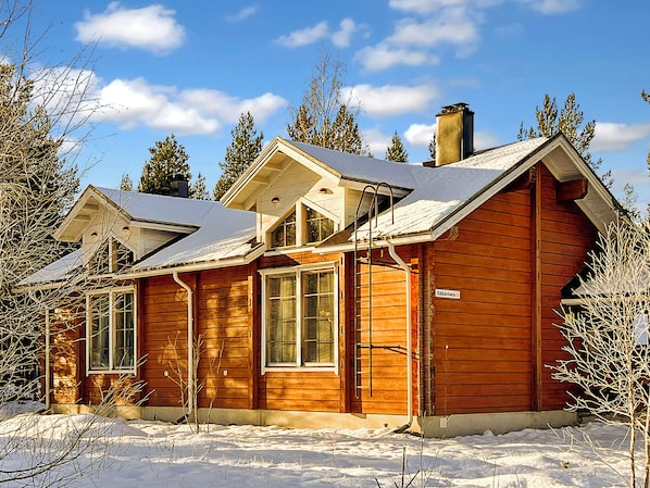 A wooden cabin with a gabled roof, large windows, and a chimney.