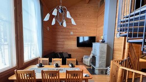 Un intérieur en bois comprenant une table à manger, des chaises, une cheminée, un téléviseur et un escalier.