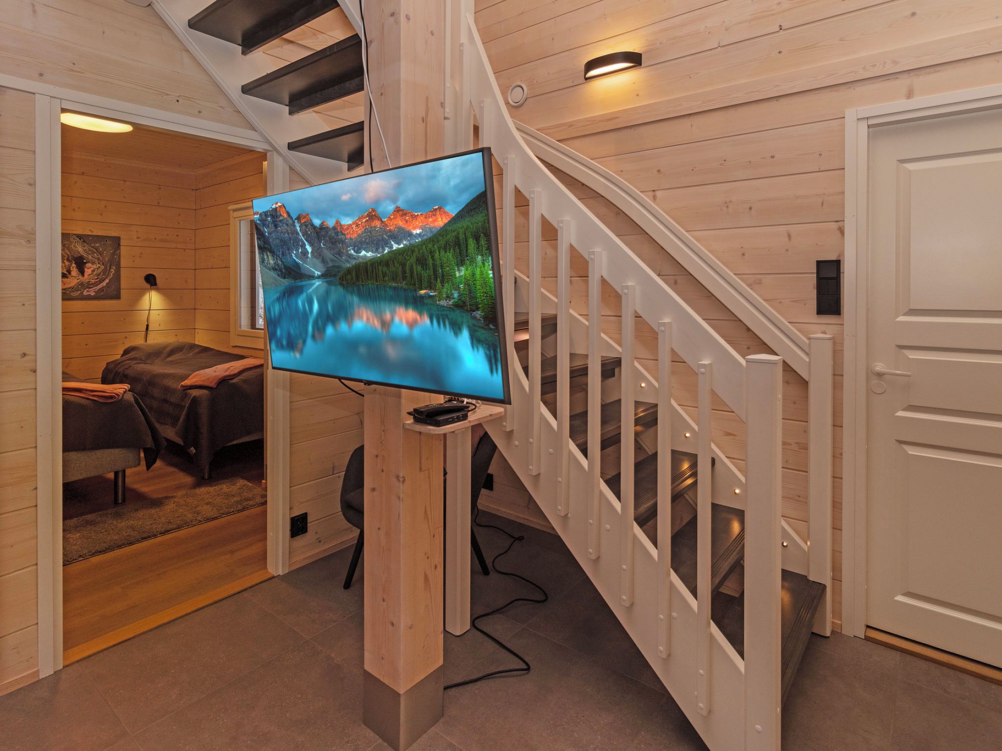 A modern interior with a wooden staircase, a flat-screen TV mounted on a wooden post, and a cozy seating area with a couch and a rug.