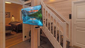 A modern interior with a wooden staircase, a flat-screen TV mounted on a wooden post, and a cozy seating area with a couch and a rug.