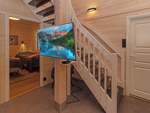 A modern interior with a wooden staircase, a flat-screen TV mounted on a wooden post, and a cozy seating area with a couch and a rug. - Mäkitie 4 by Interhome (Kuusamo)