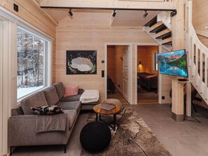 A cozy cabin interior with a sofa, a round coffee table, a painting, and a TV on a wooden wall.