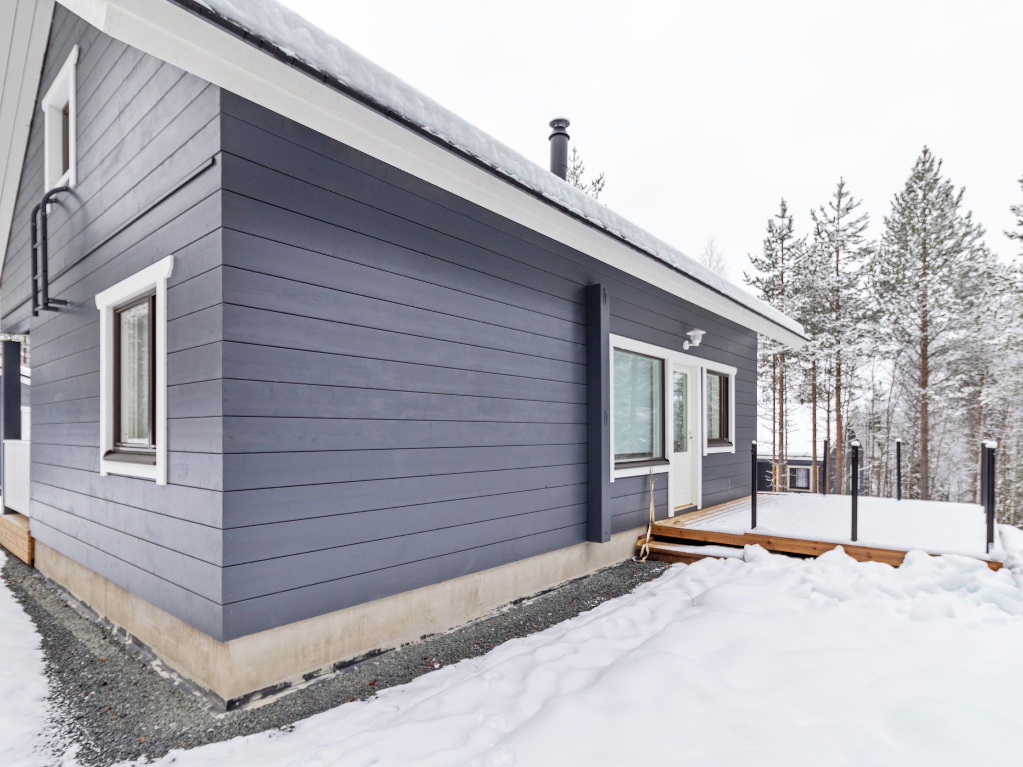 Une maison moderne à deux étages, avec une façade grise, un porche à l’avant et un paysage enneigé.
