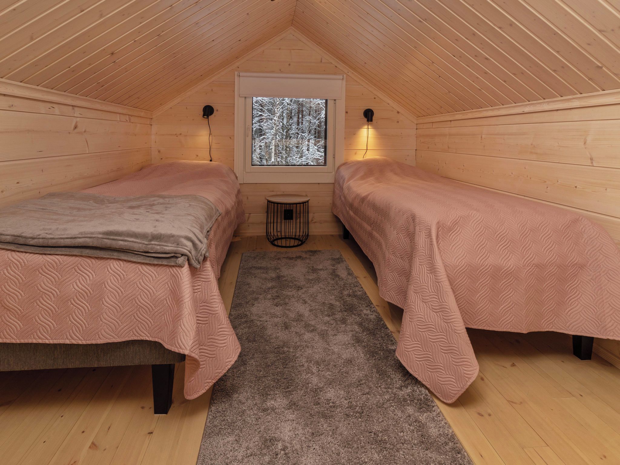 A cozy attic bedroom with two beds, a window with a view of trees, and a small round table.