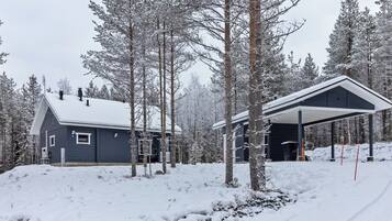 Une cabane enneigée dotée d’un espace extérieur abrité, entourée d’arbres.