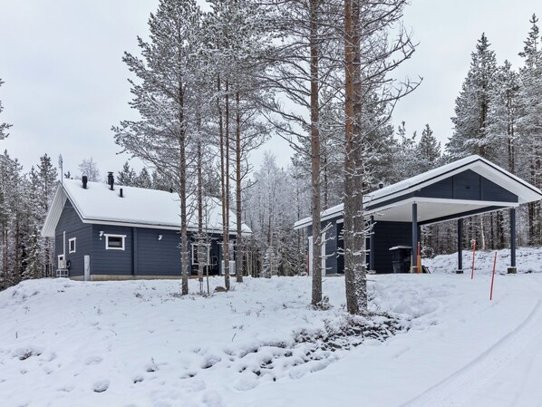 A snow-covered cabin with a covered outdoor area, surrounded by trees.