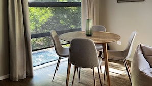 A modern dining area with a round table, four chairs, and a large window with curtains. - Pheasant Lodge - a touch of luxury in the countryside (Upper Moutere)