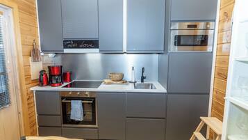 Une cuisine compacte avec des meubles gris, un four en acier inoxydable, une machine à café et un tableau noir servant de menu.