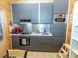 Une cuisine compacte avec des meubles gris, un four en acier inoxydable, une machine à café et un tableau noir servant de menu.