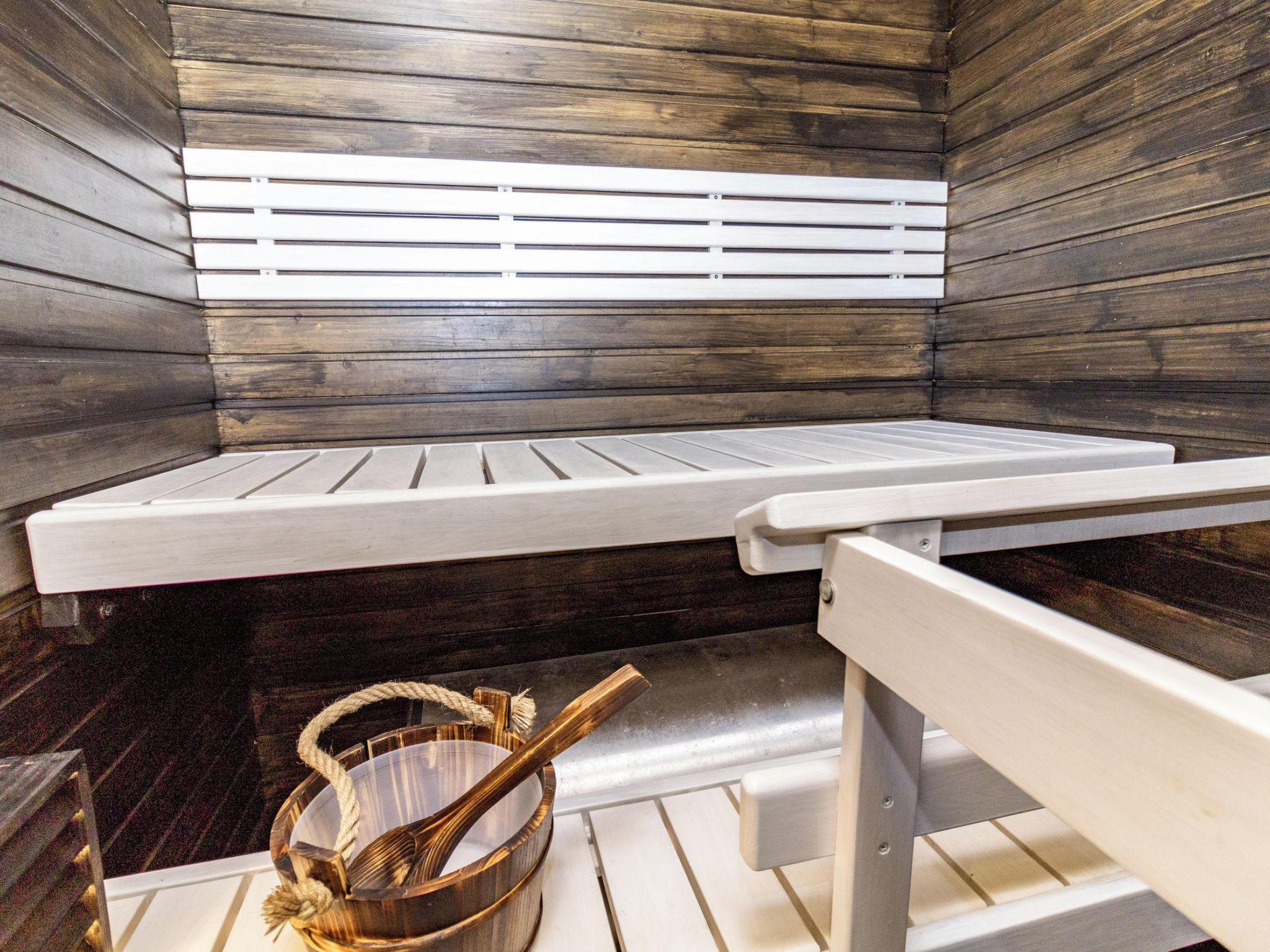 Un sauna avec un banc et un seau en bois.