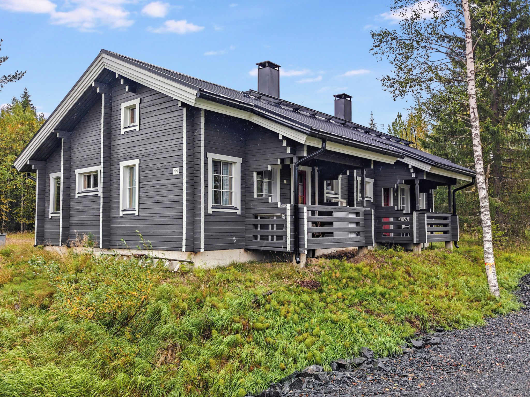 A two-story cabin with a porch, surrounded by natural vegetation.