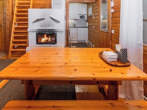 A wooden interior with a fireplace, a kitchen area, and a dining table.
